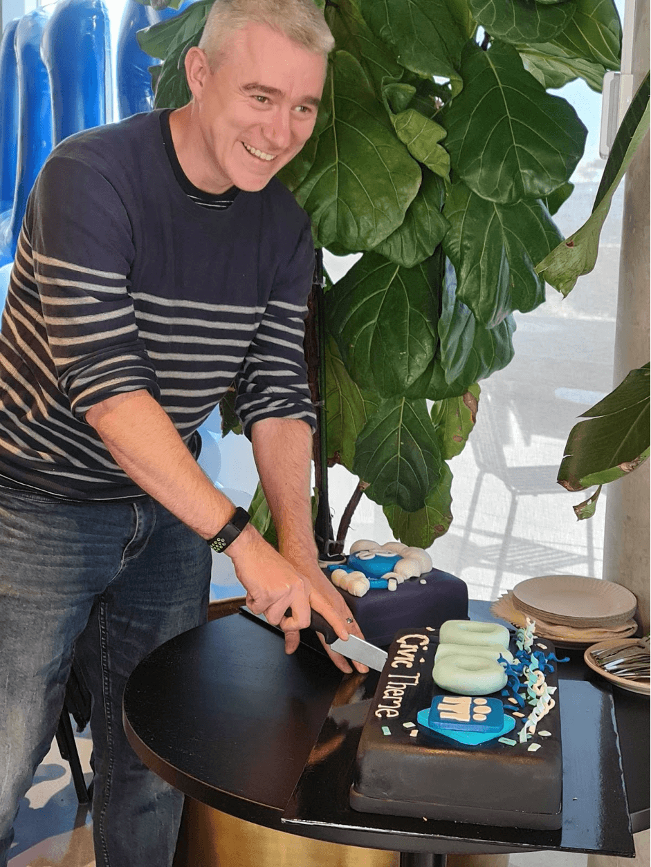 A guy in blue stripes shirt cutting the cake at the Drupal 10 launch party and Melbourne December Drupal Meetup